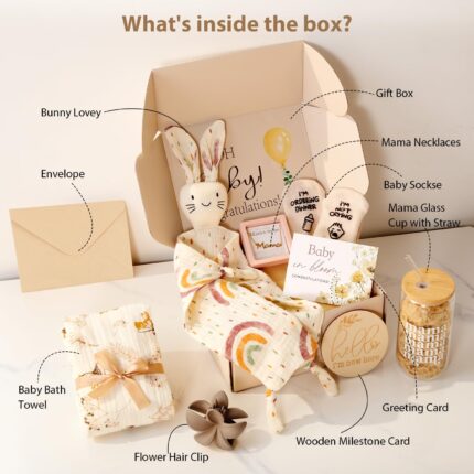 An elegant gift box containing a silver necklace, glass cup, flower hair clip, bunny lovey, baby bath towel, baby socks, and