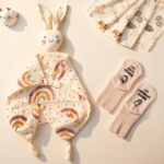 An elegant gift box containing a silver necklace, glass cup, flower hair clip, bunny lovey, baby bath towel, baby socks, and