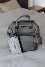 Grey Inclusive LittleOnes diaper bag backpack with a changing station unfolded, showing baby essentials and a pacifier case.